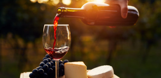 Pouring red wine into the glass in the vineyard at sunset