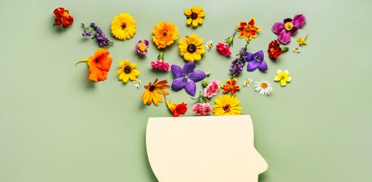 Mental health concept. Paper cut human head symbol and flowers on a green background