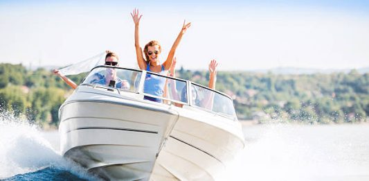 Group of young people with raised hands enjoying in a speedboat ride.